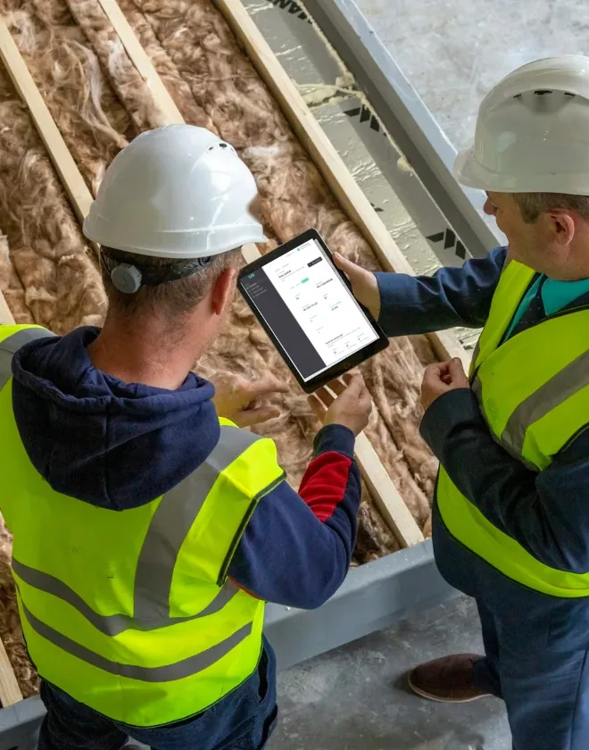 Dois engenheiros de capacete consultam um tablet em uma obra